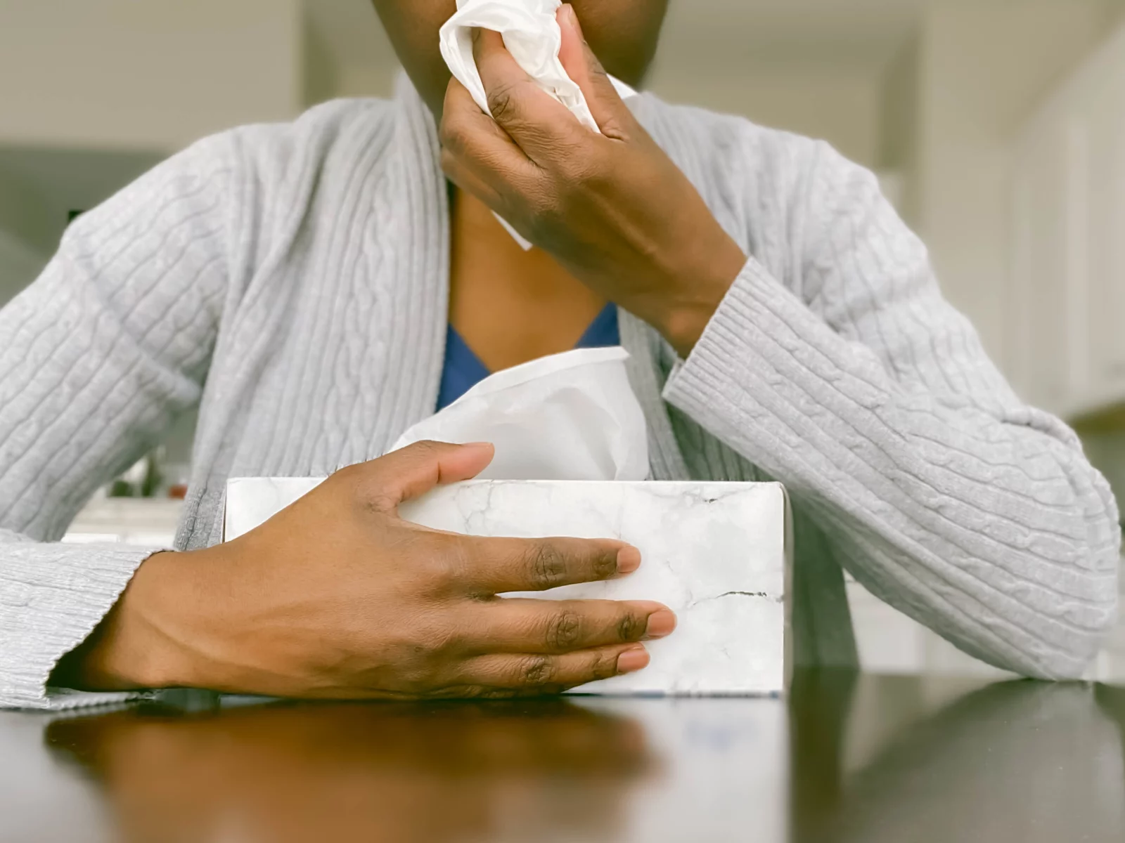 Image of someone blowing their nose with a box of tissues in front of them